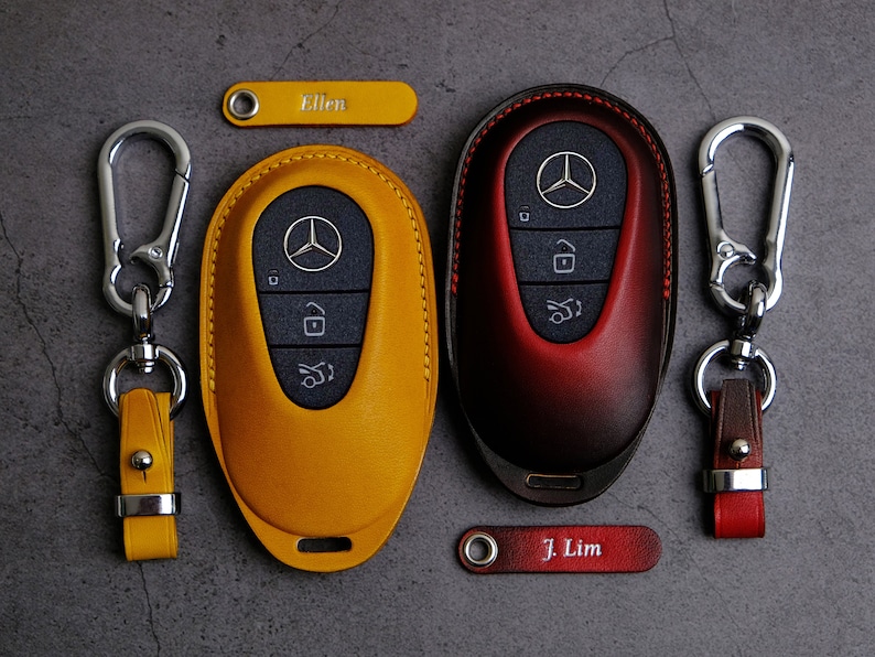 May include: Two leather keychains with key fobs, one yellow and one red, with the Mercedes-Benz logo. The keychains have the names "Ellen" and "J. Lim" engraved on them.