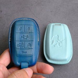 May include: Two leather key fobs, one blue with a car key design and the other light blue with a stylized figure holding a gun.