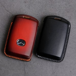 May include: Two leather key fobs, one red and one black, with stitched edges. The red key fob has a silver Mazda logo.