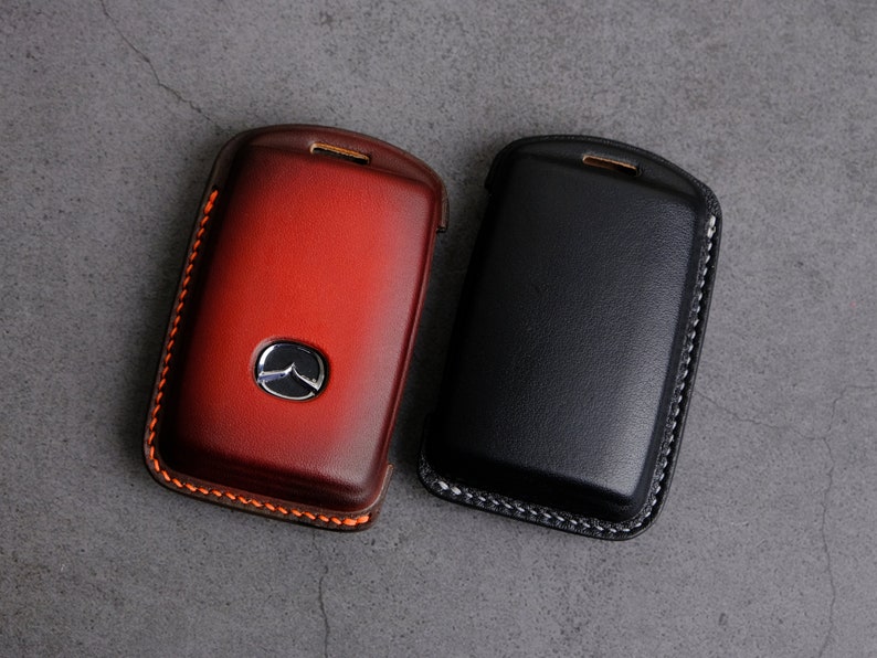 May include: Two leather key fobs, one red and one black, with stitched edges. The red key fob has a silver Mazda logo.