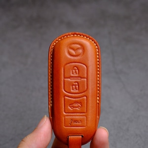 May include: A brown leather key fob with a Mazda logo and buttons for lock, unlock, trunk, and hold.