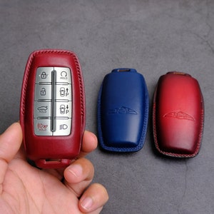May include: Three leather key fobs, one red, one blue, and one red with a gradient. The red key fob has a silver key with buttons and the text "HOLD".