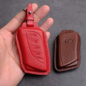 May include: Two leather key covers, one red and one brown. The red cover has a Lexus logo and buttons. The brown cover has a Lexus logo.