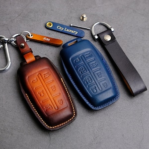 May include: Two leather key covers, one brown and one blue, with a silver key chain and a small leather strap with the text "Cey Luxury" on it.