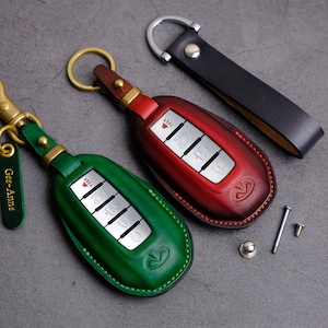 May include: Two leather key fobs, one green and one red, with silver buttons and a car logo. The key fobs are attached to keychains with metal rings and a black leather strap.