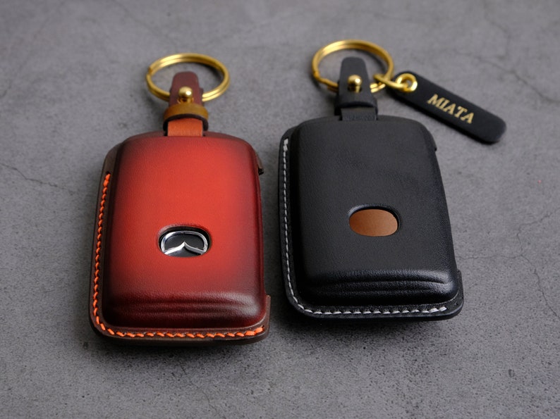 May include: Two leather keychains with gold key rings. One keychain is red with a Mazda logo and the other is black with white stitching. The black keychain has a gold tag that says "MIATA".