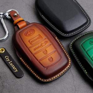 Puede incluir: Tres fundas de llaves de cuero en diferentes colores. La primera es marrón con costuras, la segunda es negra con costuras y la tercera es verde con costuras. La funda de llave marrón tiene el texto "Cey Luxury".