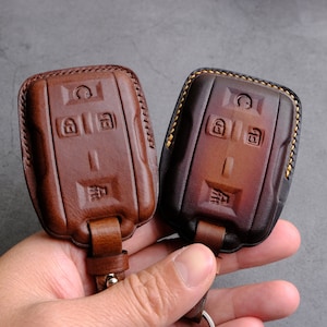 May include: Two brown leather key fobs with stitching around the edges. The key fobs have a design of four buttons on the front.