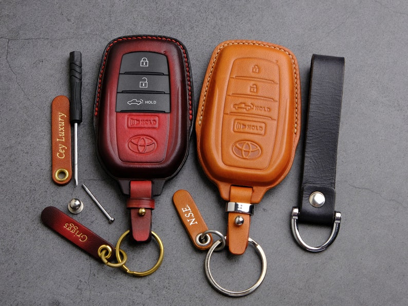 May include: Two leather key fobs with keychains. The key fobs are brown and red and have stitching around the edges. The keychains have metal rings and leather tags that say "NISE" and "CHESS".