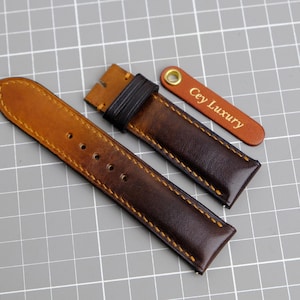 May include: Two brown leather watch straps with contrasting stitching. The strap on the left is a lighter brown and the strap on the right is a darker brown. The strap on the right has a small leather tag with the text "Cey Luxury" in gold lettering.
