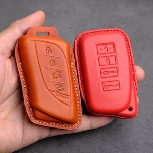 Puede incluir: Dos llaveros de cuero, uno marrón y otro rojo, con varios botones y la palabra "HOLD" impresa en ellos.