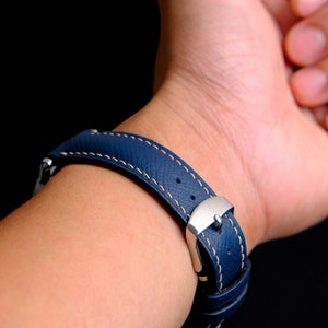 May include: A dark blue leather watch strap with white stitching and a silver buckle.