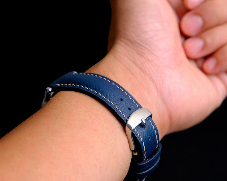 May include: A dark blue leather watch strap with white stitching and a silver buckle.