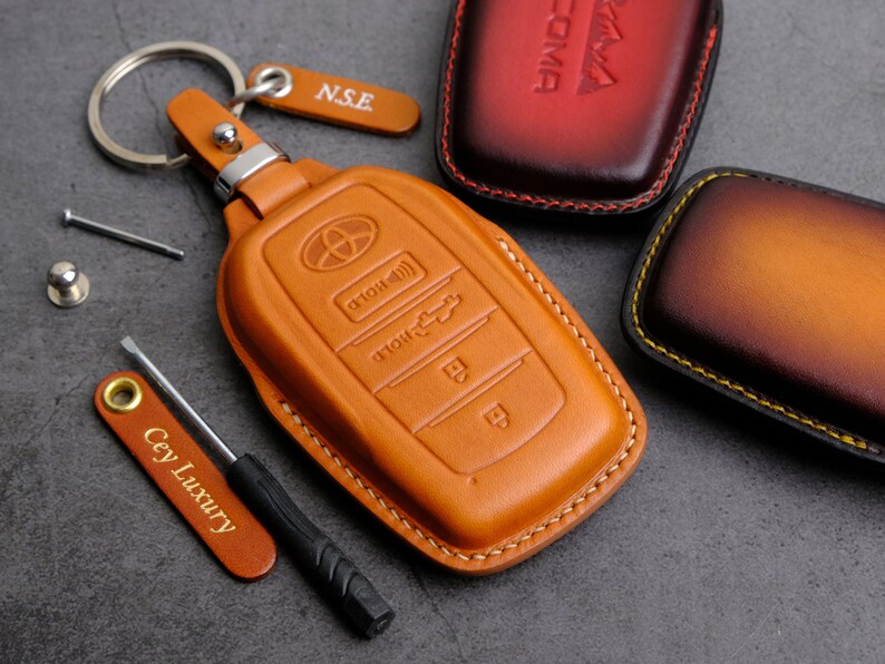 May include: A brown leather key fob with a key ring and a small screwdriver. The key fob has a Toyota logo and buttons labeled "Hold" and "Unlock".