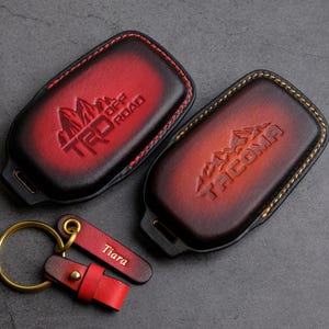 May include: Two red leather keychains with the words "TRD OFF ROAD" and "TACOMA" embossed on them. The keychains are attached to a gold key ring with a red leather fob that says "Tiara".