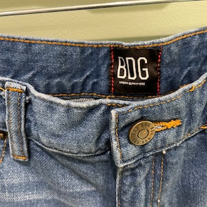 K&ouml;nnte beinhalten: Eine blaue Jeanshose mit einem braunen Leder-Patch, auf dem "BDG Urban Outfitters" steht.