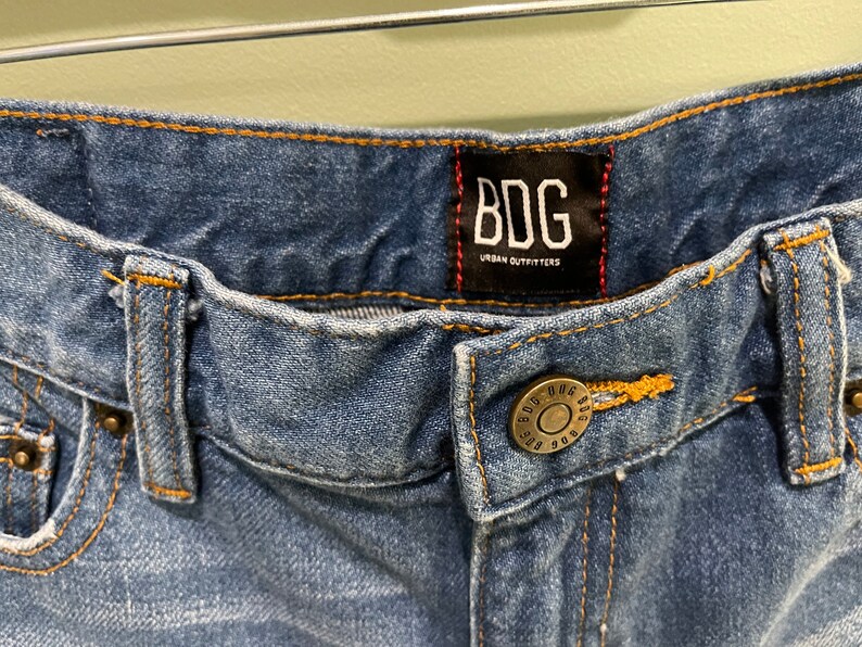 K&ouml;nnte beinhalten: Eine blaue Jeanshose mit einem braunen Leder-Patch, auf dem "BDG Urban Outfitters" steht.