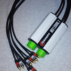 May include: A white audio amplifier with black text that reads "TARAMPS MD1200.1". The amplifier has two green knobs and is connected to six black RCA cables with gold connectors.