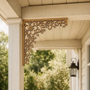 Könnte beinhalten: Ein brauner Eckwinkel aus Holz mit einem komplizierten, lasergeschnittenen Blumen- und Rankenmuster. Das dekorative architektonische Element ist in der oberen Ecke zwischen einem vertikalen Verandapfosten und einem horizontalen Balken montiert.