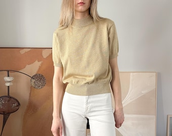 May include: A light beige mock neck sweater with short sleeves. The sweater has a subtle speckled pattern and a ribbed hem.