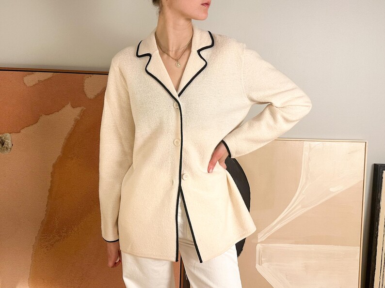 May include: Cream-colored blazer with black trim. The long-sleeved jacket has a notched collar and three buttons. The blazer is paired with white pants.