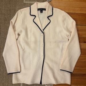 May include: Cream-colored button-down jacket with black trim. The jacket has a collar and three buttons down the front. The brand name "JOSEPHINE CHANS" is visible on the label.