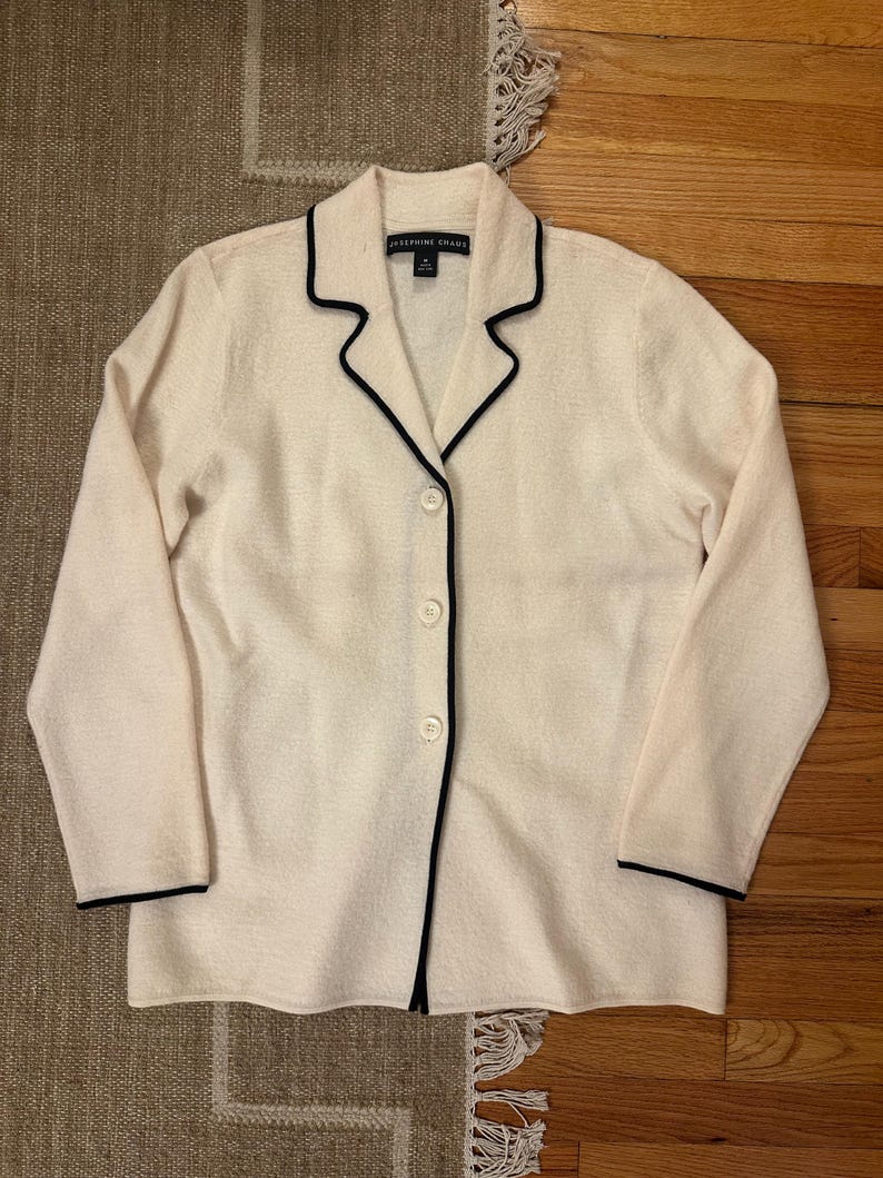 May include: Cream-colored button-down jacket with black trim. The jacket has a collar and three buttons down the front. The brand name "JOSEPHINE CHANS" is visible on the label.