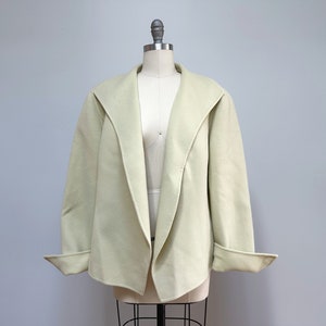May include: A light green, open-front jacket with long sleeves and a shawl collar. The jacket is made of a soft, textured fabric.