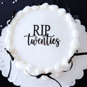 May include: White cake with black frosting and a black topper that says "RIP twenties".
