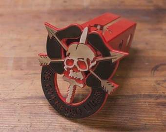 May include: A red and black desk organizer featuring a skull and arrows emblem. The emblem has a gold skull with red eyes and the text "DE OPPRESSO LIBER" in black. The organizer is made of wood and has a slot for holding items.