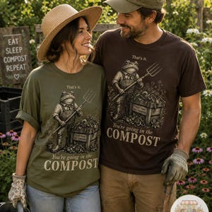 Könnte beinhalten: Ein olivgrünes T-Shirt und ein dunkelbraunes T-Shirt, jeweils mit einer Grafik eines Frosches, der eine Heugabel neben einer Kiste hält. Der Text lautet: That's it. You're going in the COMPOST. Auf der Kiste steht: TRASH TODAY, SOIL TOMORROW.