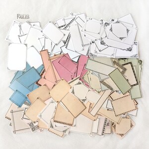 Pu&ograve; includere: Una grande collezione di cornici decorative in carta di vari colori e design, tra cui blu, verde, rosa e beige. Le cornici sono perfette per lo scrapbooking, la creazione di biglietti e altri progetti di artigianato.