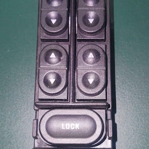 Puede incluir: Panel de control de ventanas de coche de plástico negro con seis botones para subir y bajar las ventanas y un botón con la etiqueta "LOCK".