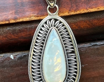 May include: A silver pendant with a white mother of pearl teardrop shaped stone set in a silver rope design.