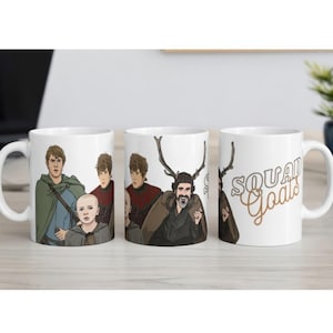 May include: Three white ceramic mugs with different illustrations. One mug features a group of cartoon characters, another has a character with antlers, and the third mug has the words "SQUAD Goals" in a brown script.