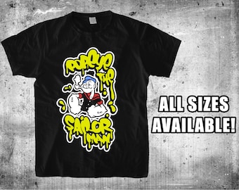 May include: Black t-shirt with a yellow and white graphic of Popeye the Sailor Man. The graphic features Popeye holding a pipe and a can of spinach. The text "Popeye the Sailor Man" is written in a dripping font.