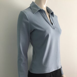 May include: A light blue long-sleeved collared shirt with a V-neck.