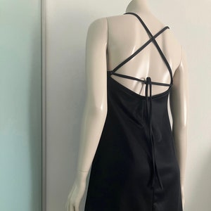 May include: A black mini dress with a criss-cross strap detail on the back. The straps tie at the back of the neck.