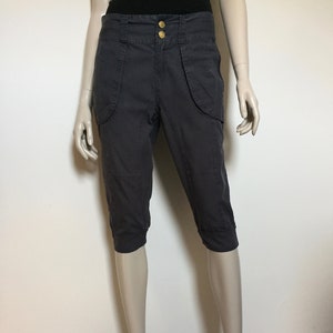 May include: Dark gray cropped pants with a high waist and two front pockets. The pants have a button closure and a zipper fly.