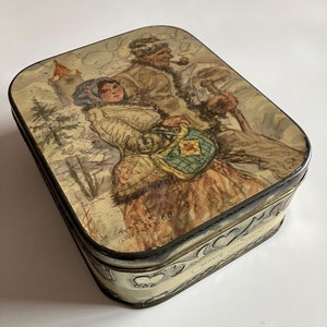 May include: Vintage tin box with a painted scene of two people in winter clothing walking through a snowy landscape. The box has a decorative border and the text "Germany" on the side.