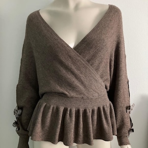 May include: A brown ribbed knit sweater with a V-neck and a ruffled hem. The sleeves have bows on the cuffs.
