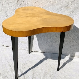 May include: A wooden side table with a unique, asymmetrical, freeform top and black metal legs. The table is made of light wood and has a natural finish.