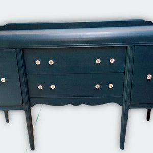 May include: A teal blue vintage sideboard with two drawers and two doors. The sideboard has crystal knobs and sits on four legs.
