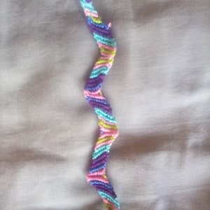 May include: A colorful friendship bracelet with a zig-zag pattern in shades of purple, pink, blue, and green.