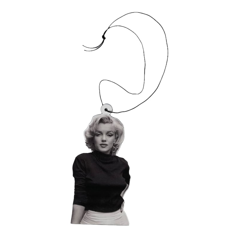 May include: Black and white photo of a woman with blonde hair wearing a black turtleneck sweater and a white skirt. The photo is attached to a black string.
