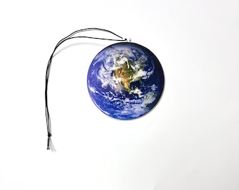 May include: A round air freshener featuring a detailed image of Earth, showcasing continents and oceans in shades of blue, green, and brown. It has a black string for hanging. The air freshener is a decorative item.