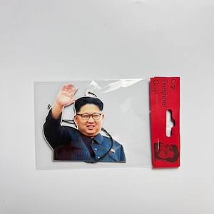 Puede incluir: Un ambientador de coche con una foto de un hombre con traje oscuro y gafas. El texto "Car Freshener Guy" está impreso en el embalaje rojo.