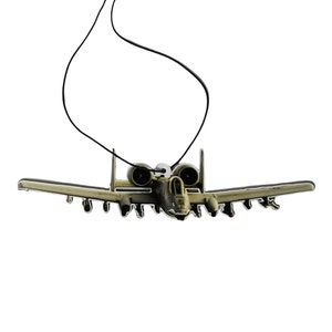 May include: A tan and green A-10 Warthog airplane air freshener with a black string for hanging.