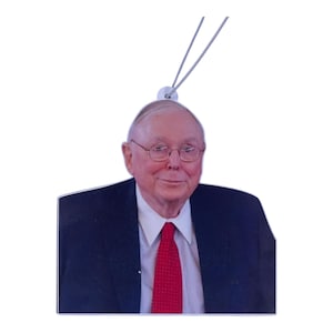May include: A rectangular ornament featuring a portrait of a man wearing glasses, a red tie, and a dark blue suit. The ornament has a silver string for hanging. The background is white.