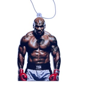 May include: A car air freshener featuring a photo of Mike Tyson wearing boxing gloves. The air freshener is white with a black string for hanging. The photo shows Tyson in a boxing stance with his arms raised and his fists clenched. The text "TYSON" is printed on his boxing shorts.